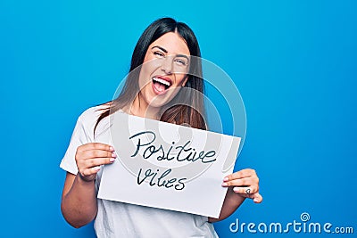 Young beautiful woman asking for optimist attitude holding paper with positive vibes message looking positive and happy standing Stock Photo