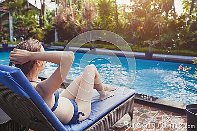 Beautiful woman in bikini relaxing in deck chair near swimming pool in hotel Stock Photo