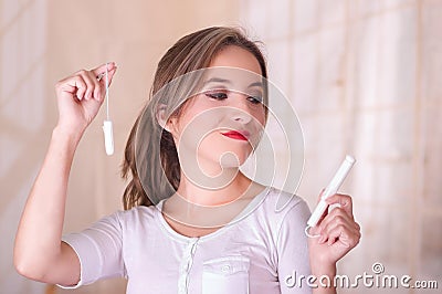 Young beautiful woman with a bored face, holding a menstruation cotton tampon in her hand, in a blurred background Stock Photo