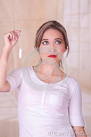 Young beautiful woman with a bored face, holding a menstruation cotton tampon in her hand, in a blurred background Stock Photo