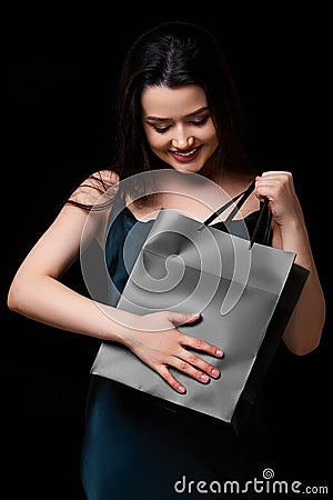 A young beautiful woman in a dark green dress with a black paper shopping bag in her hands. on a black isolated background Stock Photo