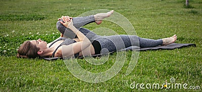 Young beautiful woman doing yoga exercise in green park near the pond. Exercices for improve the flexibility. Wellbeing Stock Photo