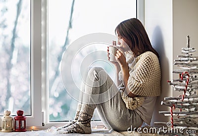 Young beautiful woman drinking hot coffee sitting on window sill Stock Photo