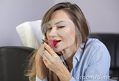 Young, beautiful woman eating strawberries. Relaxing home, desire face expression and romantic pose. Stock Photo