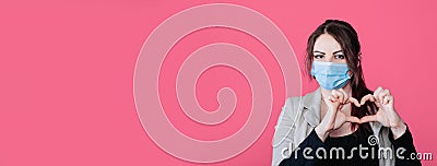 Young beautiful woman in face medical mask shows heart jesture, pink background, copy space. Stock Photo