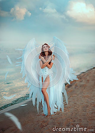 Young beautiful woman fallen angel stands on the sea beach enjoy nature. Creative sexy costume, huge artificial bird Stock Photo