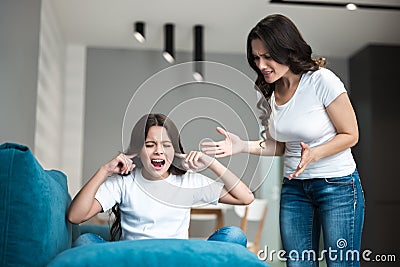 Young beautiful woman having an argument with her teen daughter shouting loud in the living room child sitting with her Stock Photo