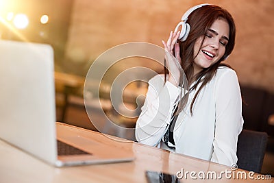 Young beautiful woman in headphones listening her favourite music from laptop feeling free while waiting her lunch in the cafe Stock Photo