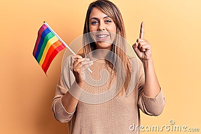 Young beautiful woman holding lgtbq flag smiling with an idea or question pointing finger with happy face, number one Stock Photo