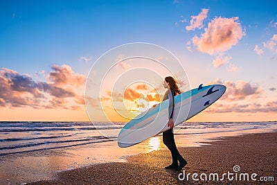 Young beautiful woman with long hair. Surf girl with surfboard on a beach at sunset or sunrise. Surfer and ocean Stock Photo