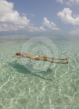 Young beautiful woman lying and floating on back in turquoise sea water on tropical paradise beach in Bora Bora Island, French Stock Photo