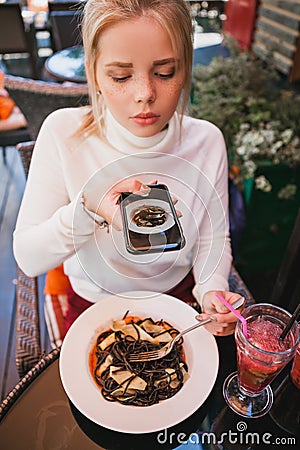 Young beautiful woman making photo of black pasta with seafood and cuttlefish ink Stock Photo