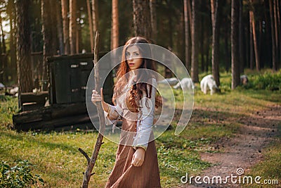 Young beautiful woma in medieval cowboy clothes, with a stick in hand. Barefoot on the ground. Against the background of the fores Stock Photo