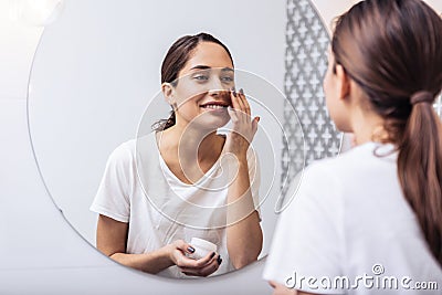 Young beautiful woman putting face cream on her nice healthy skin Stock Photo