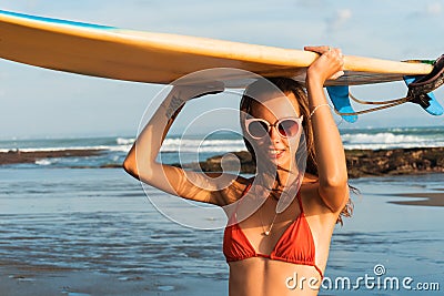 Young beautiful woman in red bikini and sun glasses holds in hands a surf on the ocean beach at sunset. Stock Photo
