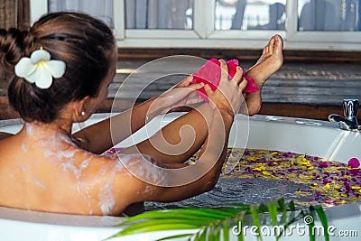 Young beautiful woman relaxing in bath with foam and tropical flowers petals,tropical flowers petals in eco hotel Bali Stock Photo