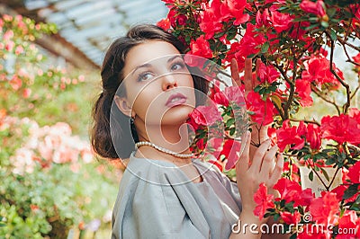 Beautiful adult girl in an azalea greenhouse dreaming in a beautiful retro dress and hat Stock Photo