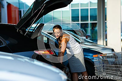 Young beautiful woman shifts the purchase from shopping cart in Stock Photo
