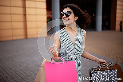 Young beautiful woman shopaholic walks out the shopping center with a pack of bags with purchases. Pink shopper in the hand of an Stock Photo