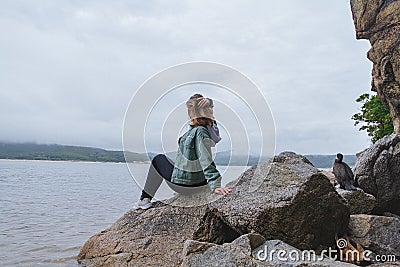 Young beautiful woman sits on the rocks on the seashore Stock Photo