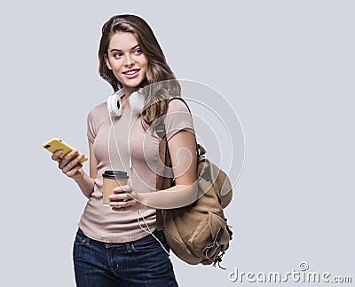Young beautiful woman with smart phone. Smiling student girl going on a travel. Isolated on gray background Stock Photo