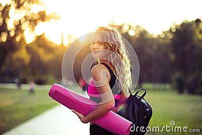 Young beautiful woman in sportswear. She`s holding a training mat. Going to do sports training, gymnastics. Outdoors Stock Photo