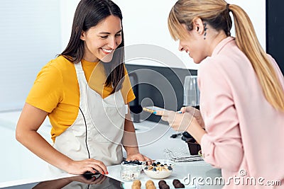 Young beautiful woman taking a photo of the healthy dishes prepared by young professional nutritionist in the kitchen at home Stock Photo