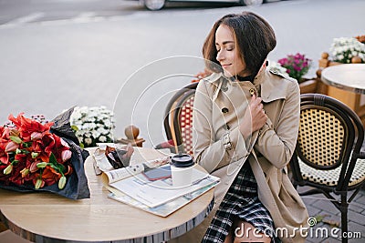 Young beautiful woman in trench coat drinking coffee in a street cafe Stock Photo