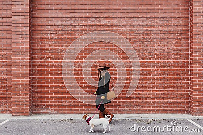 Young beautiful woman walking with her dog by the street. Orange brick wall background. Love and pets outdoors Stock Photo