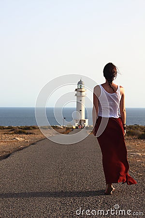 Young beautiful woman walking slowly to Cap de Barberias lighthouse during an amazing summer sunset Stock Photo