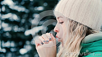 A young beautiful woman warms her hands against the backdrop of a winter snowy park Stock Photo