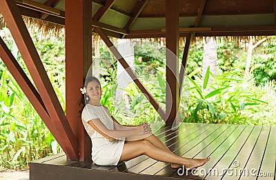 Young and beautiful woman in white dress. Woman posing in exotic Thai bungalow. Resting and traveling concept. Stock Photo