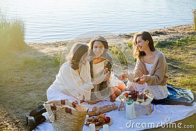 Young beautiful women of 25 years old on an autumn picnic near the lake. Glass of white wine, pastries. Happy models chatting Stock Photo