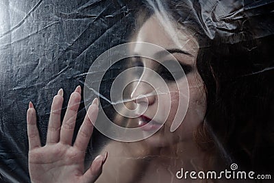 Young beauty sad woman trapped behind a plastic sheet as protection against COVID-19 Stock Photo