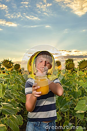 A young beekeeper holds a jar of honey in his hands in a sunflower field Stock Photo