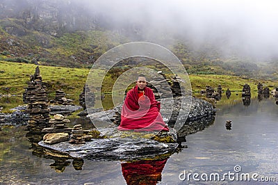 Young Bhutanese novice monk practices meditation in the centre of plateau lake , Bhutan. Editorial Stock Photo