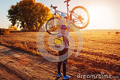 Young bicyclist raising her bicycle in autumn field. Happy woman celebrates victory holding bike in hands Stock Photo