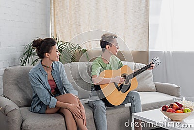 young bigender musician playing acoustic guitar Stock Photo