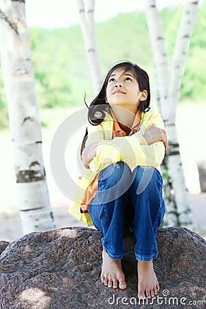 Young biracial girl sitting on rock under trees Stock Photo