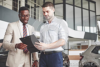 A young black businesswoman signs documents and buys a new car. The car dealer is standing next to him Stock Photo