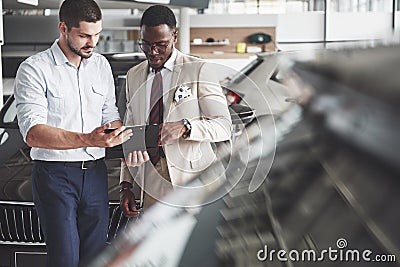 A young black businesswoman signs documents and buys a new car. The car dealer is standing next to him Stock Photo