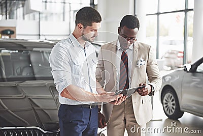 A young black businesswoman signs documents and buys a new car. The car dealer is standing next to him Stock Photo