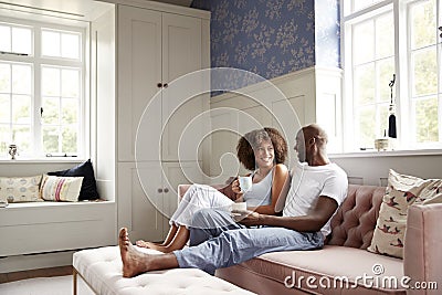 Young black couple sitting together on couch in living room drinking coffee and talking in the morning, low angle, full length Stock Photo