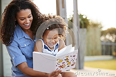 Young black girl reading book sitting on mumï¿½s knee outdoors Stock Photo