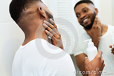 Young black man applying moisturizer on beard in bathroom Stock Photo