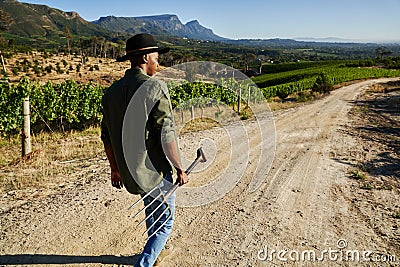 Young black man in casual clothing holding pitchfork while walking on dirt road through farm Stock Photo