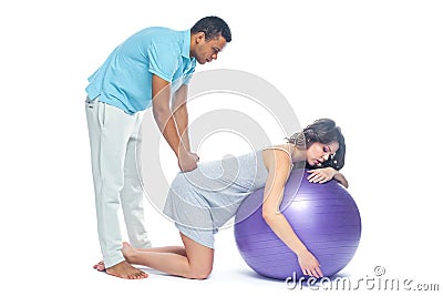 A young black man helps his white wife with birth pain with a ball. Partnered birth, partnered delivery. Isolated white Stock Photo