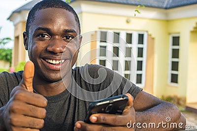 young black man holding his mobile phone smiling and giving a thumbs up Stock Photo