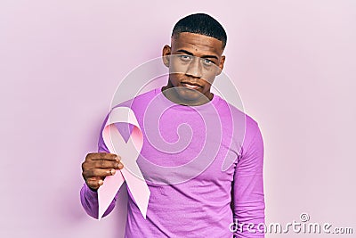Young black man holding pink cancer ribbon thinking attitude and sober expression looking self confident Stock Photo