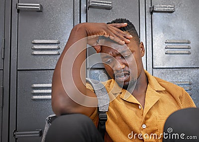 A young black man sits, head in his hand on campus looking upset, stressed Stock Photo